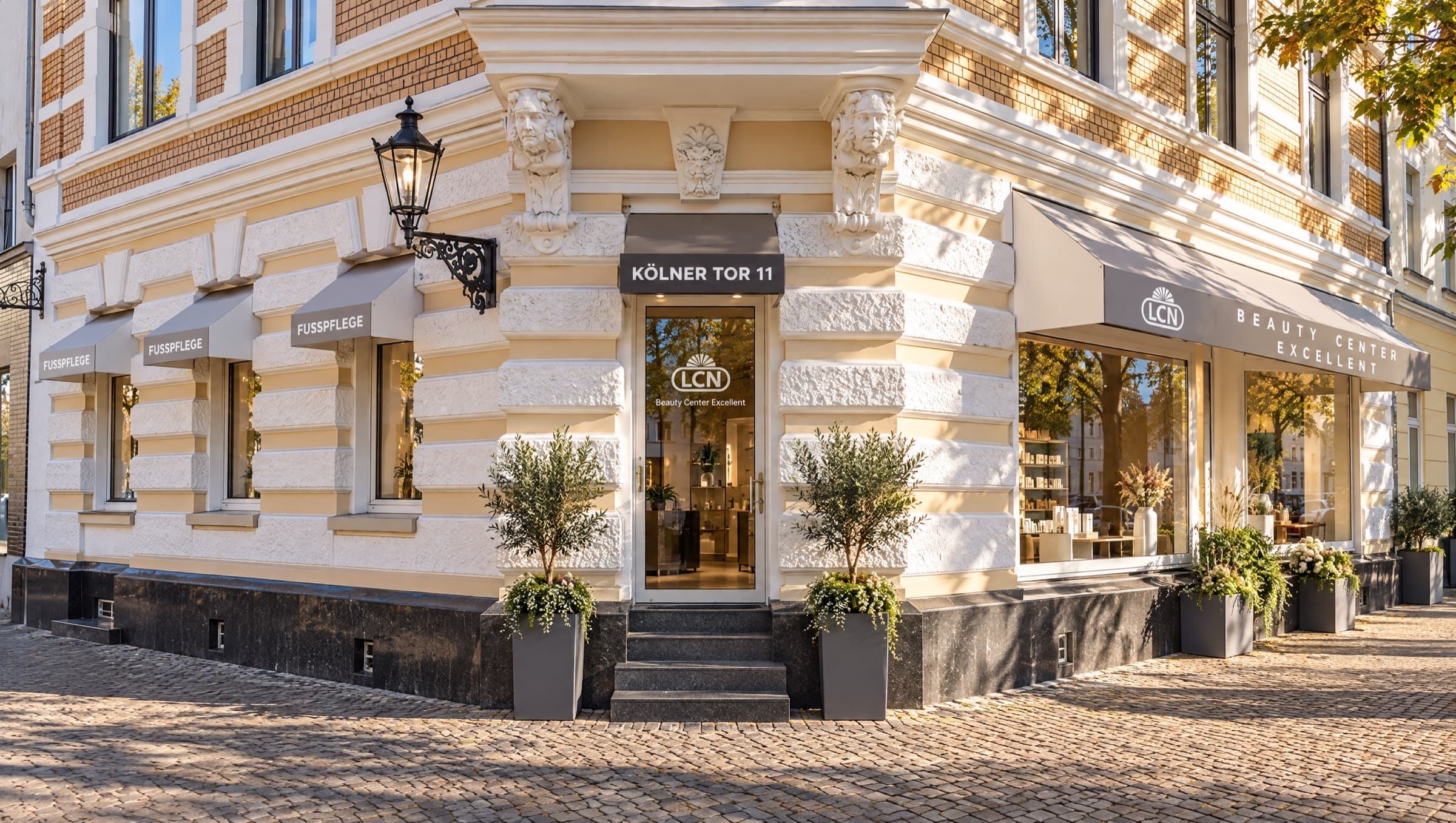 Das Eckhaus Kölner Tor 11 mit Stuckfassade: Eingangstür mit Hausnummernschild, alte Wandlaterne, Markisen „Fußpflege“ und „LCN Beauty Center Excellent“