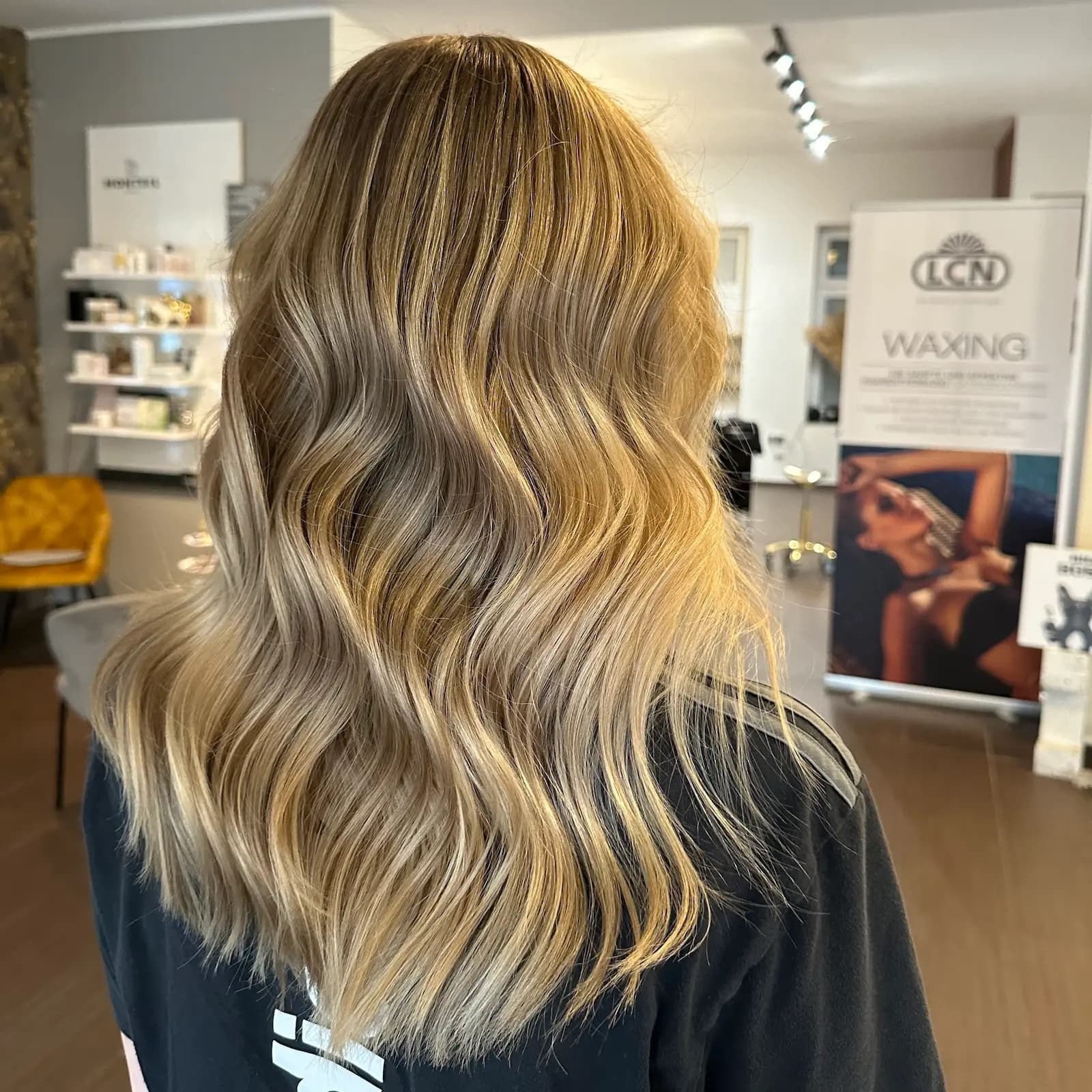 Lange blonde Haare mit Strähnchen und weichen Wellen, von hinten fotografiert