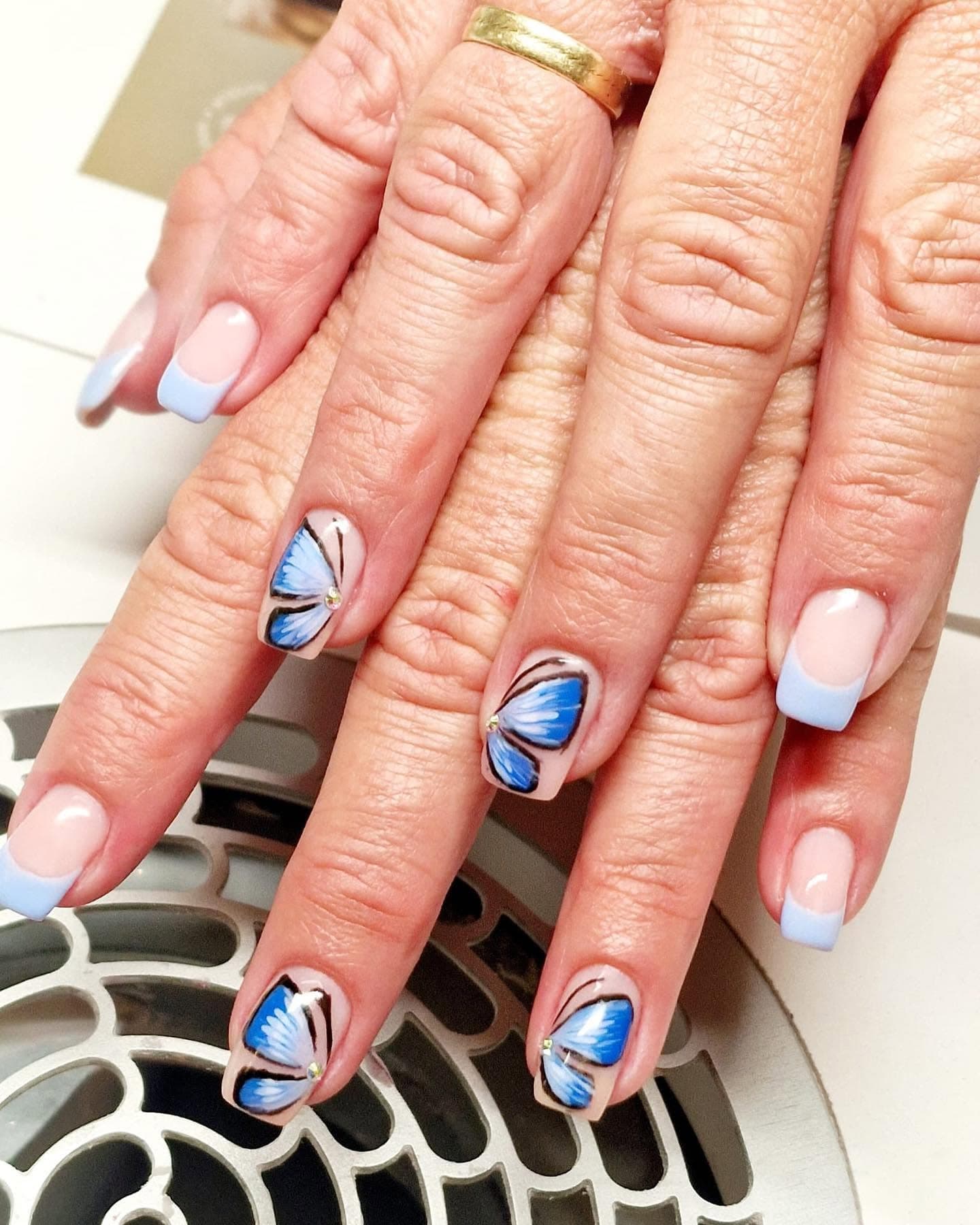 Kurze Nägel mit hellblauer French-Spitze und blauen Schmetterlingsmotiven